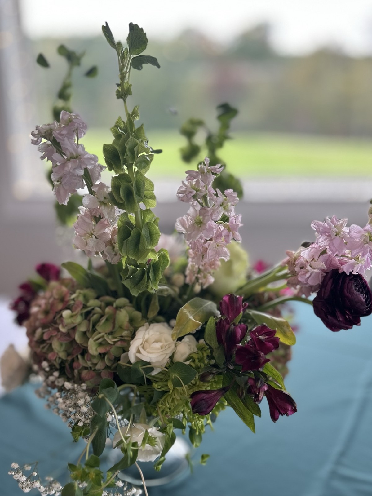 Airy pale pink and burgundy flowers arranged against a softly blurred window