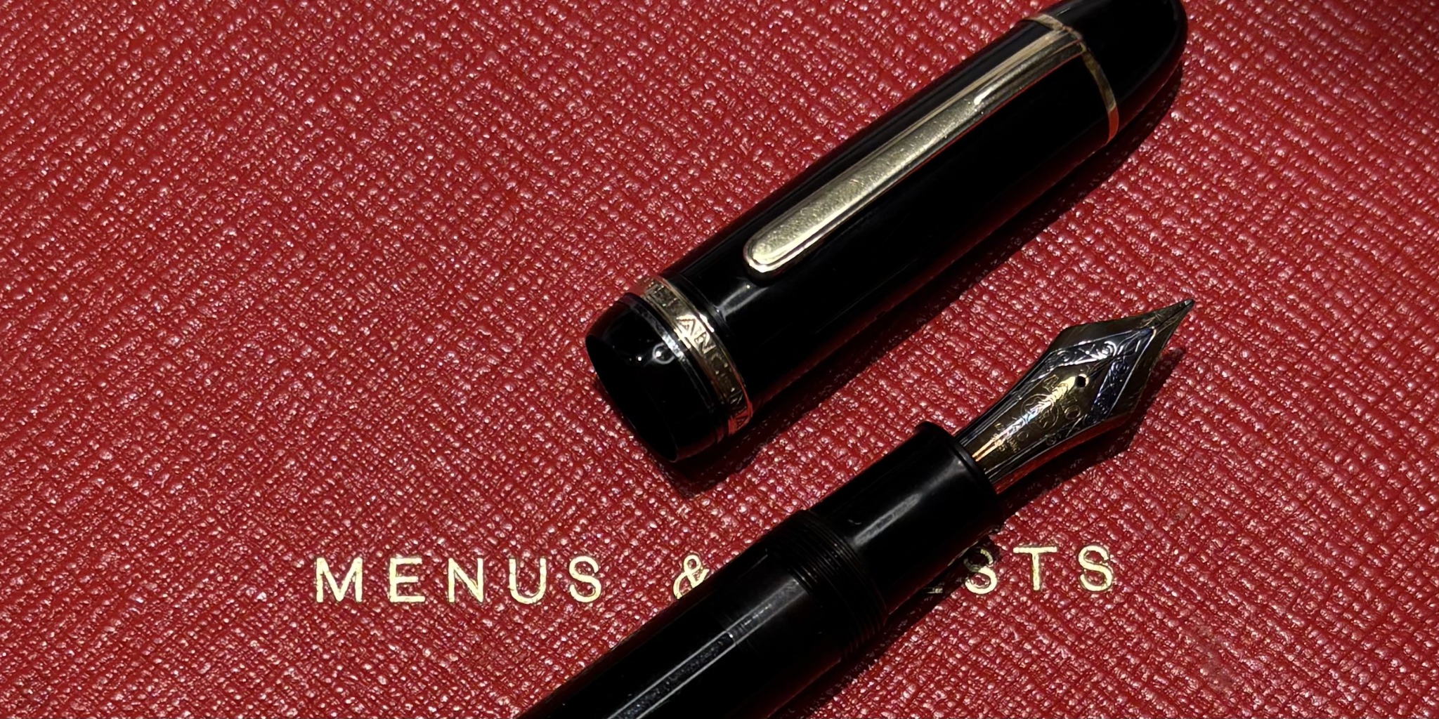 Black and gold fountain pen nib and cap on a textured red background