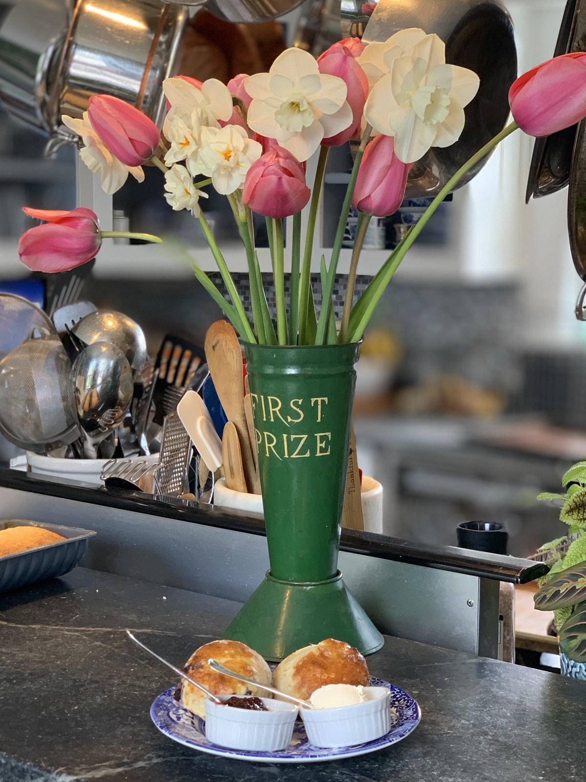 Pink tulips and white narcissus in a green trophy vase beside breakfast