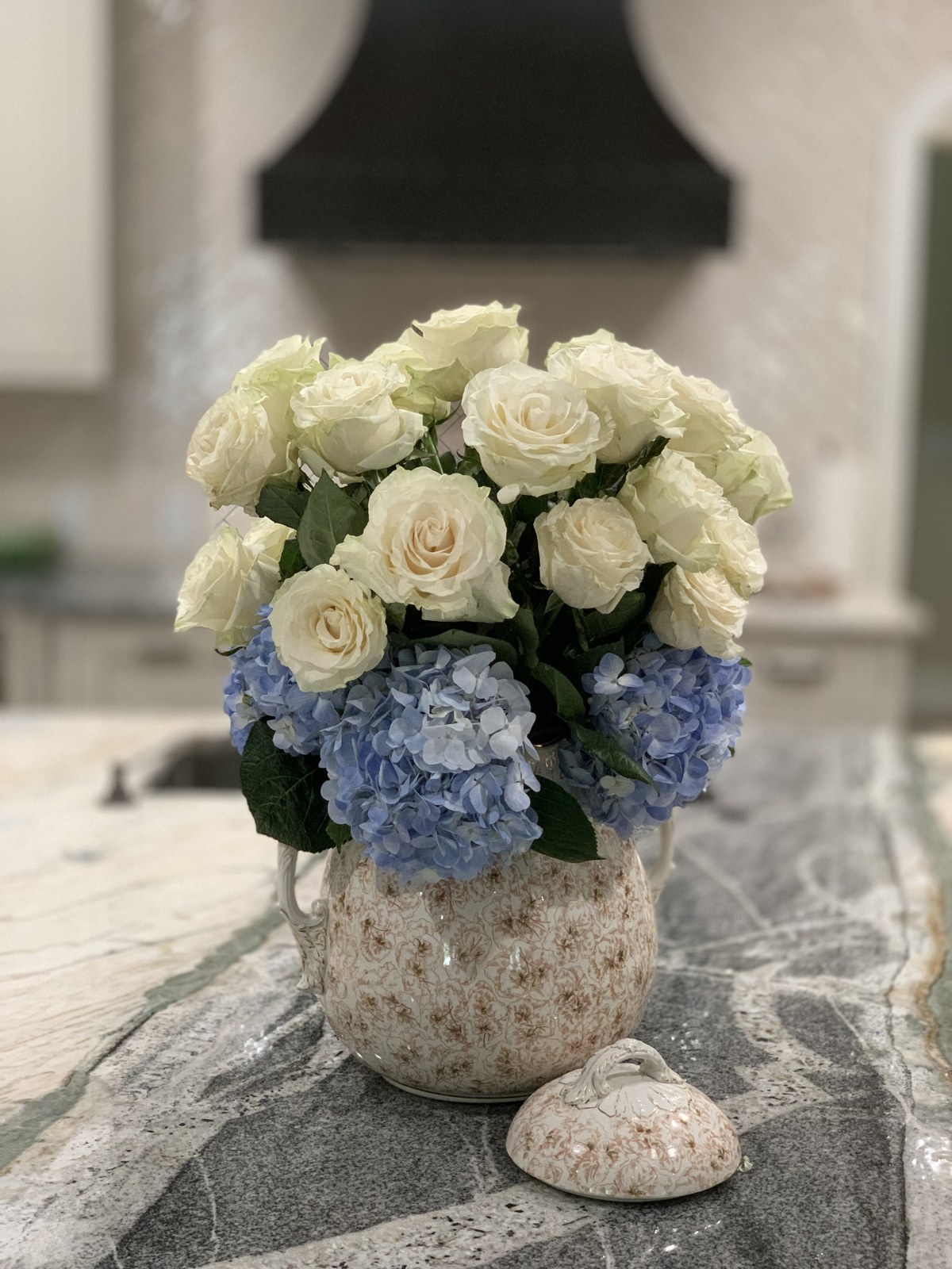 White roses and blue hydrangeas in a patterned ceramic vessel