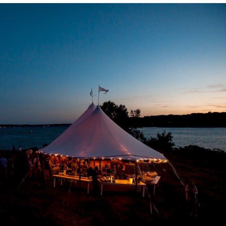A warmly lit tent beside the water at dusk