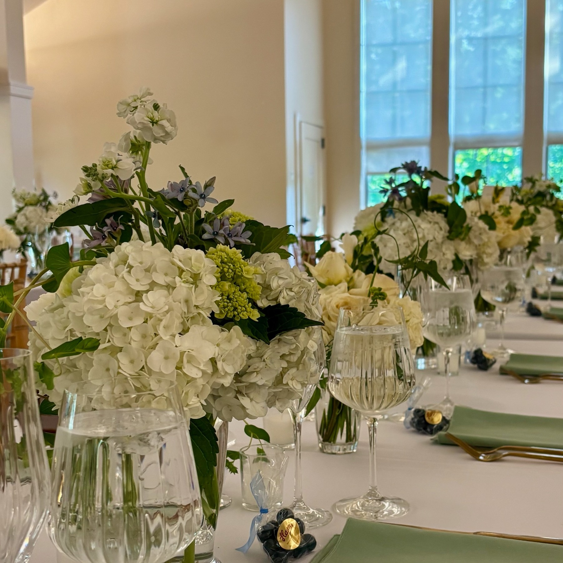 White wedding flowers, pale green linens and glassware arranged along a reception table