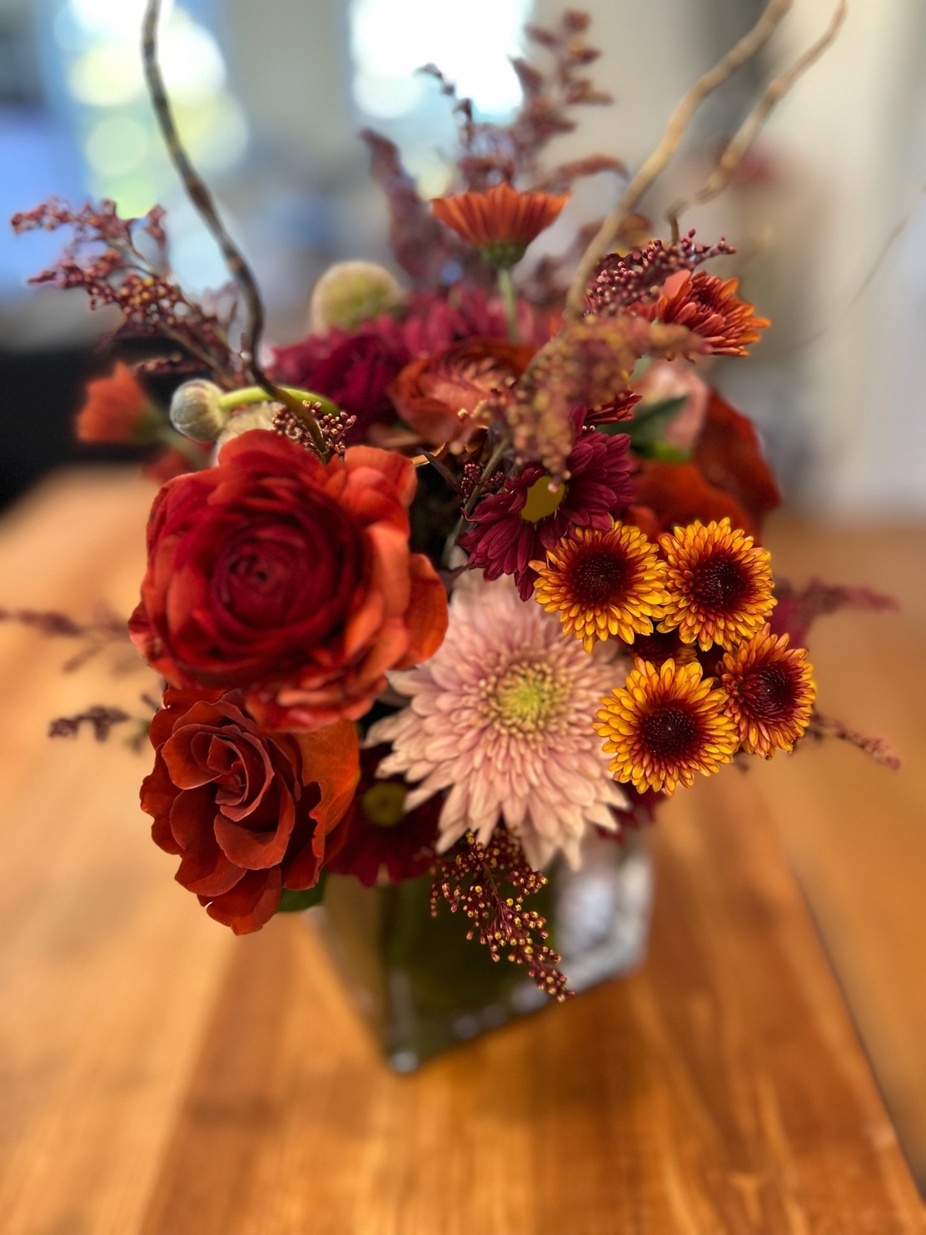 Red roses, orange flowers and pale pink chrysanthemums in a glass vase