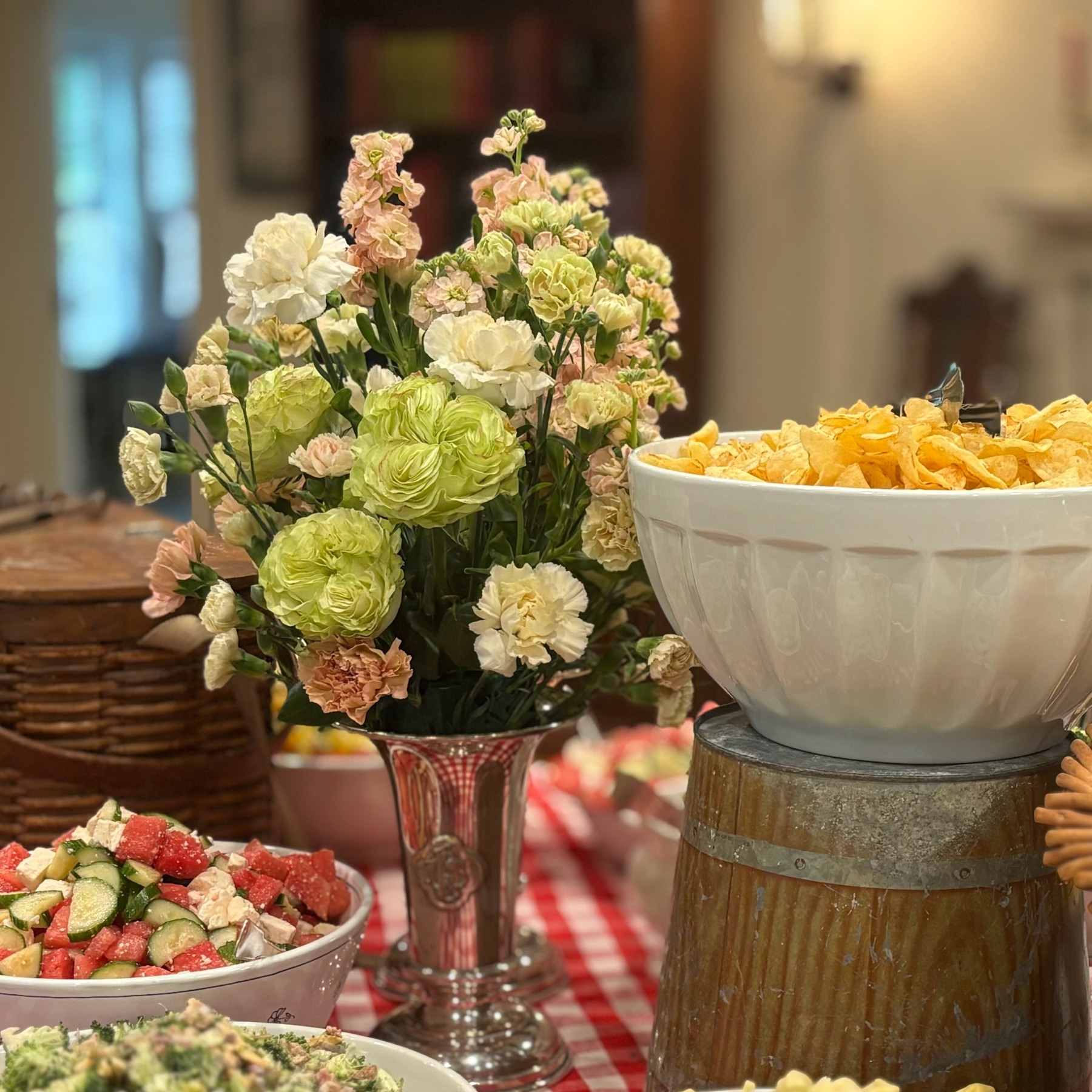Pale green and pink flowers in a tall glass vessel beside food at a buffet