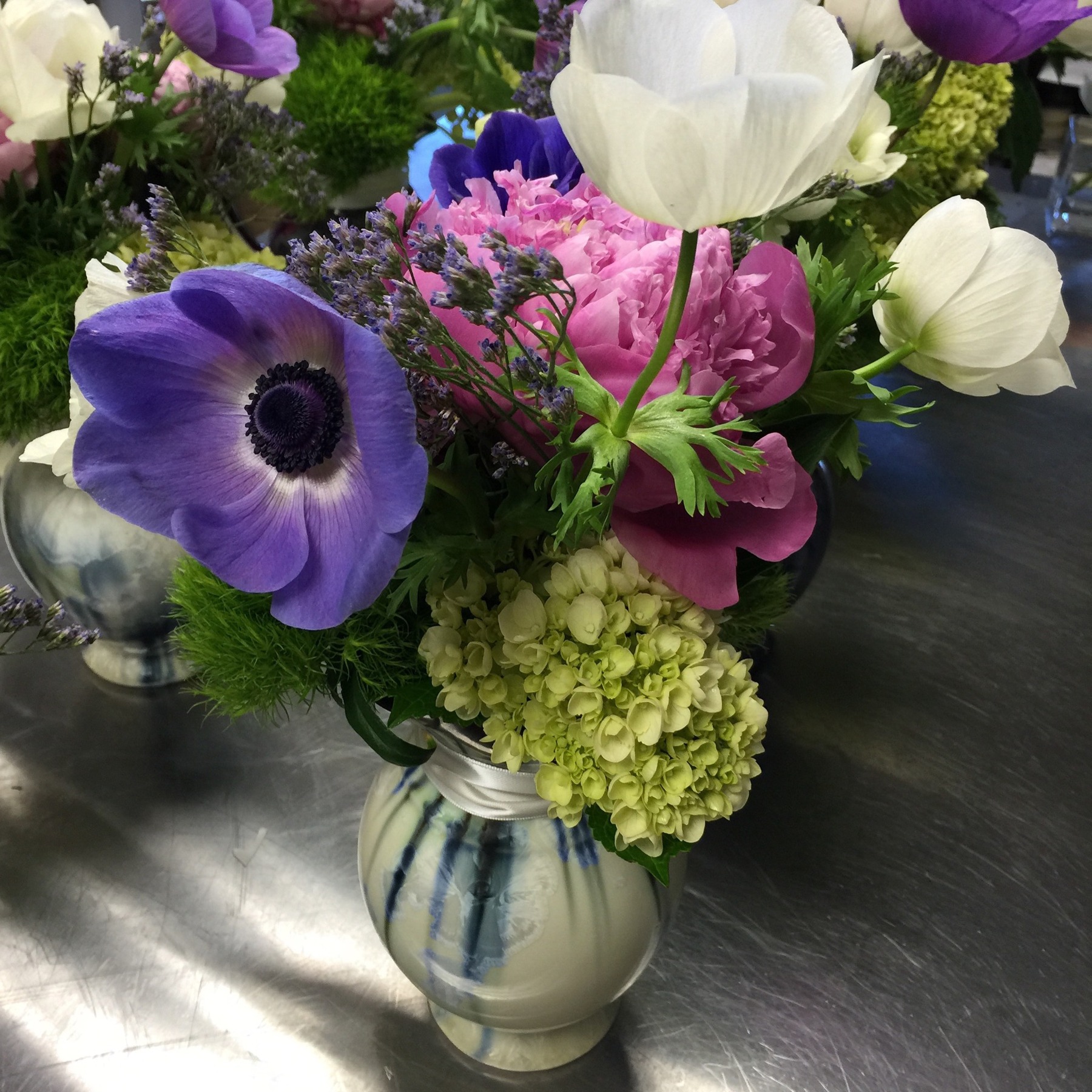 Purple and white anemones, pink peonies and green hydrangeas in a polished silver vessel