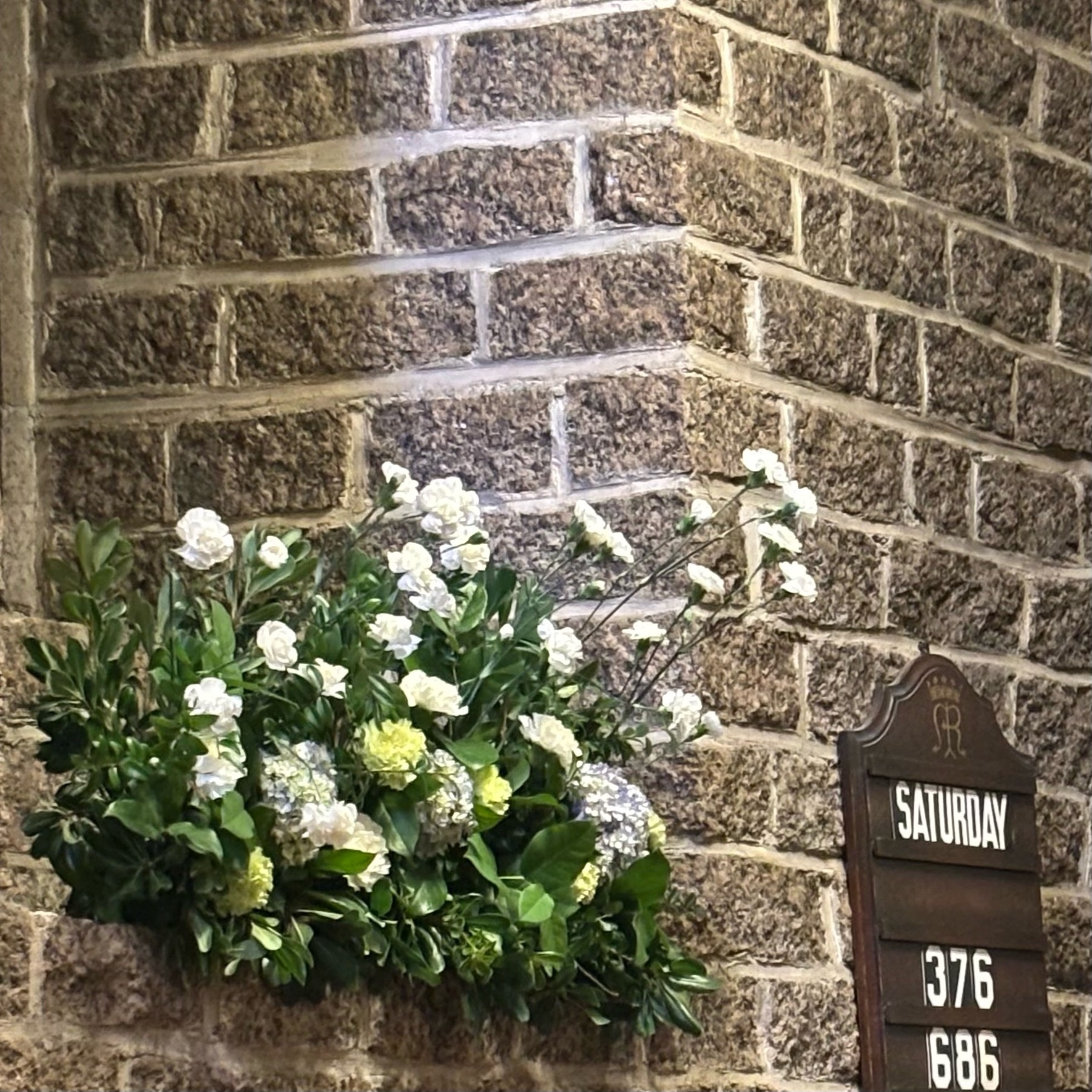 White flowers and green foliage arranged against textured church stonework
