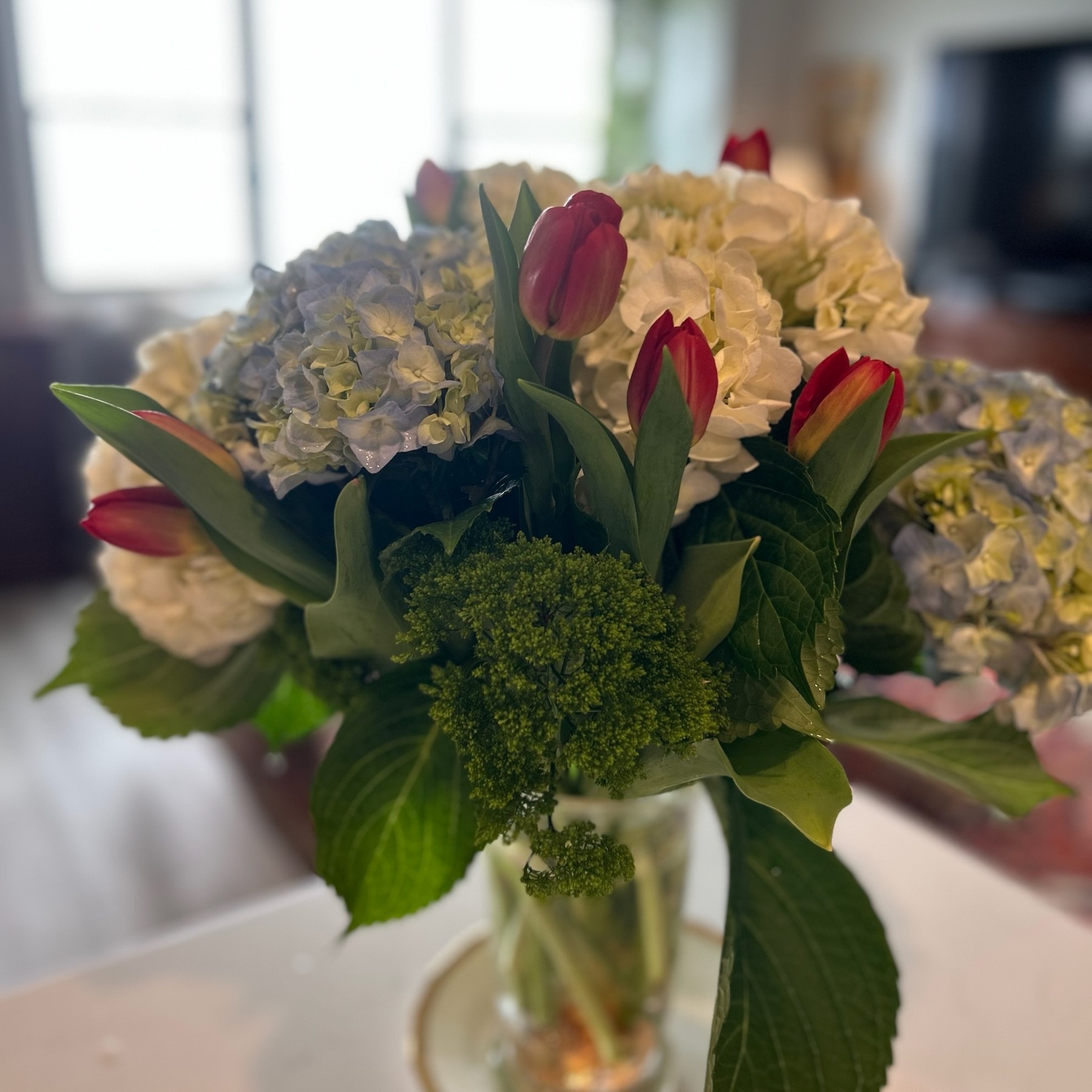 Red tulips and blue and white hydrangeas in a vintage clear glass vessel
