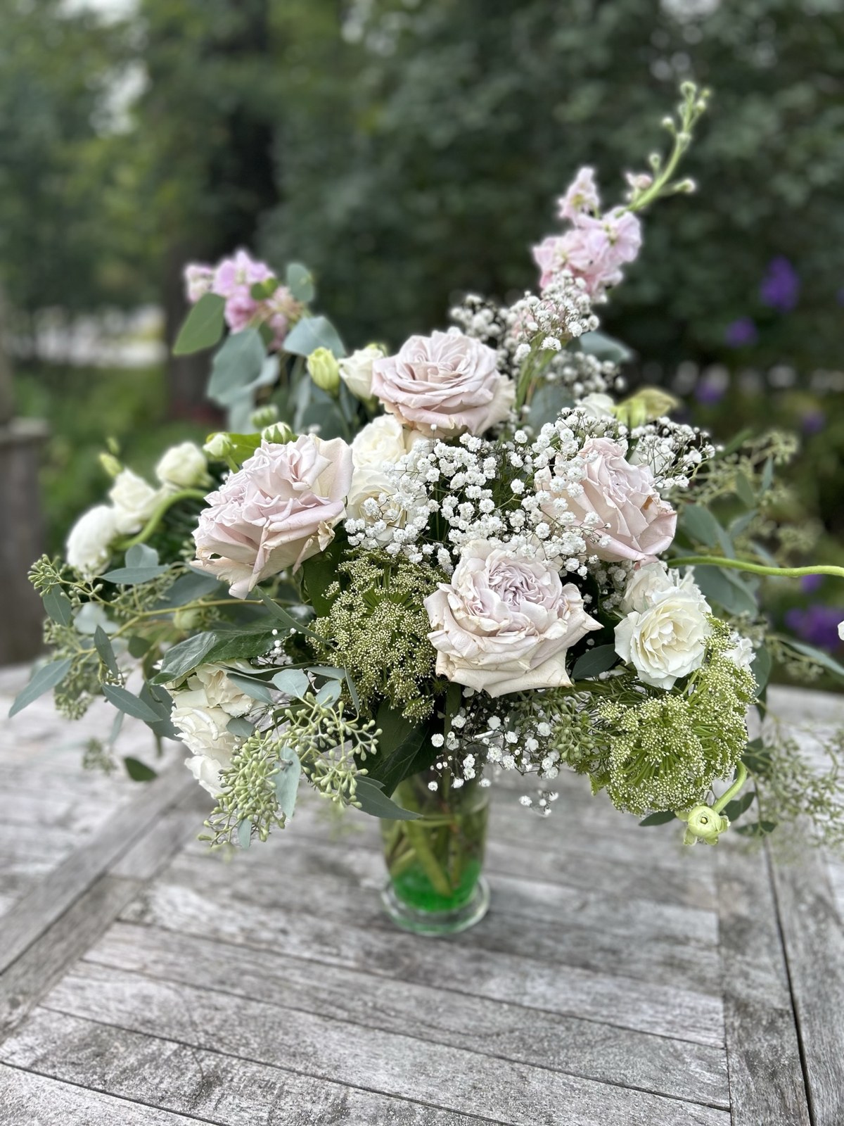 Blush roses, white flowers and greenery on a weathered garden table