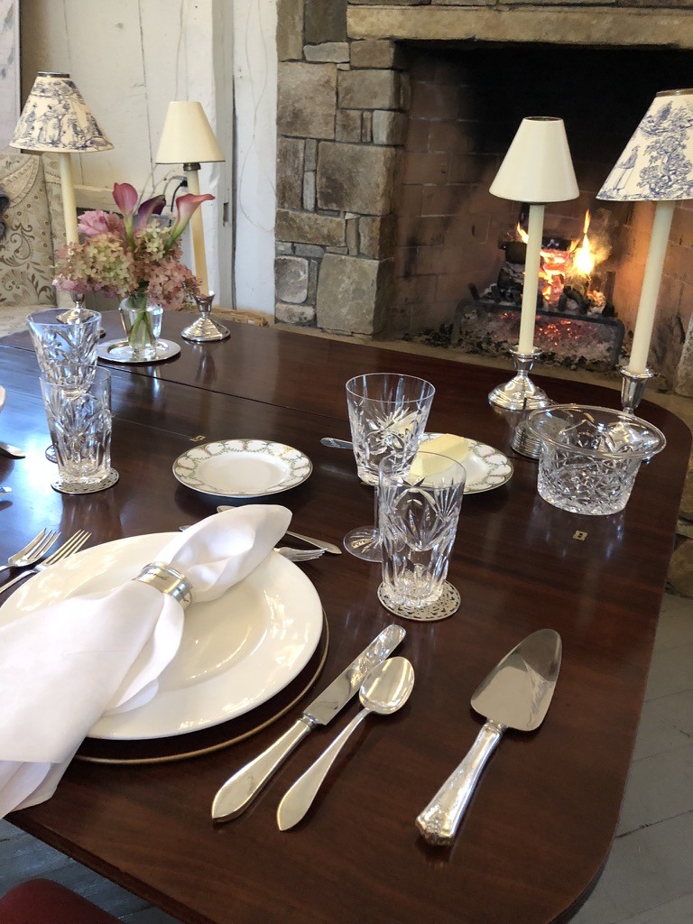A dining table with crystal glasses and flowers beside a stone fireplace