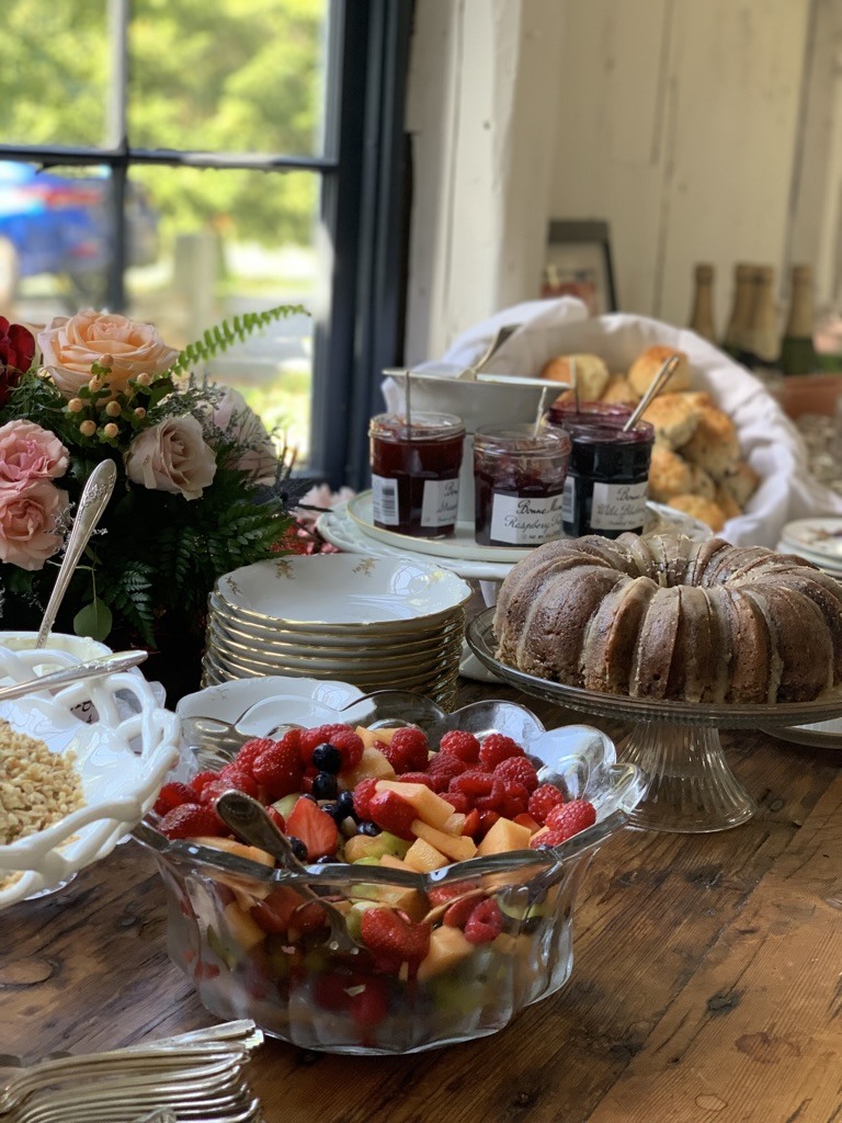 Fruit, a ring cake, preserves and flowers arranged beside a sunlit window