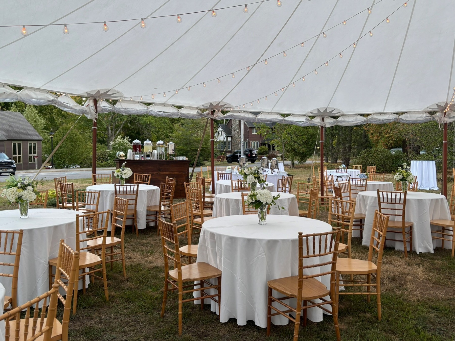 Round tables with white linens and wooden chairs beneath a garden tent
