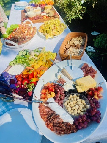 Outdoor table with colorful vegetables, cheeses, fruit and charcuterie