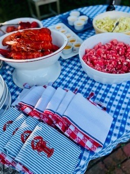 Lobster and side dishes on a blue checked tablecloth beside striped napkins