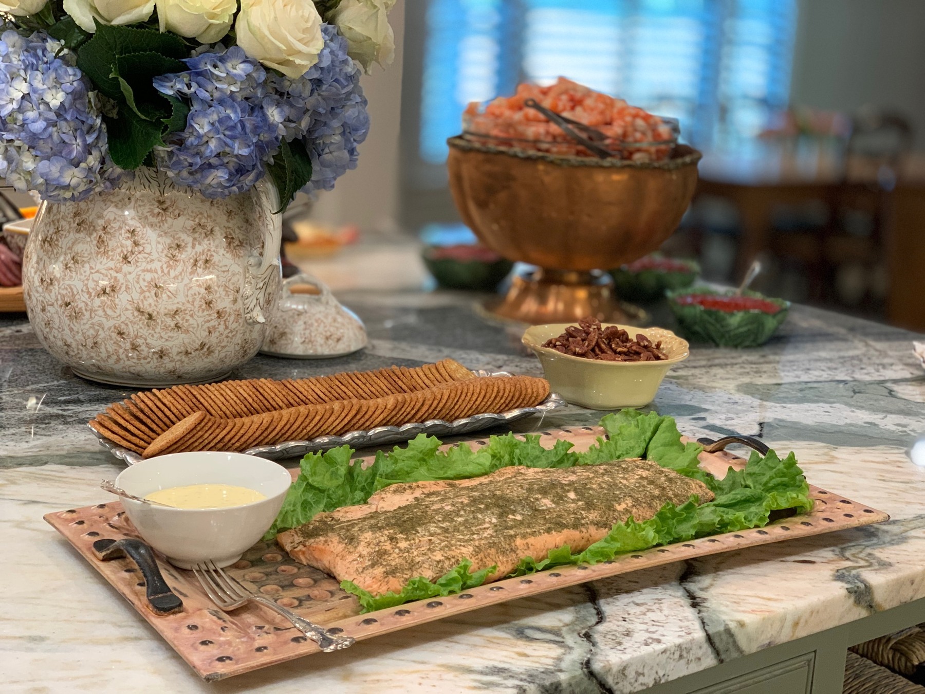 Salmon on a copper tray, shrimp in a copper bowl, and white roses with blue hydrangeas
