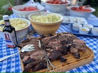 Sliced grilled steak on a wooden board beside salads and serving bowls