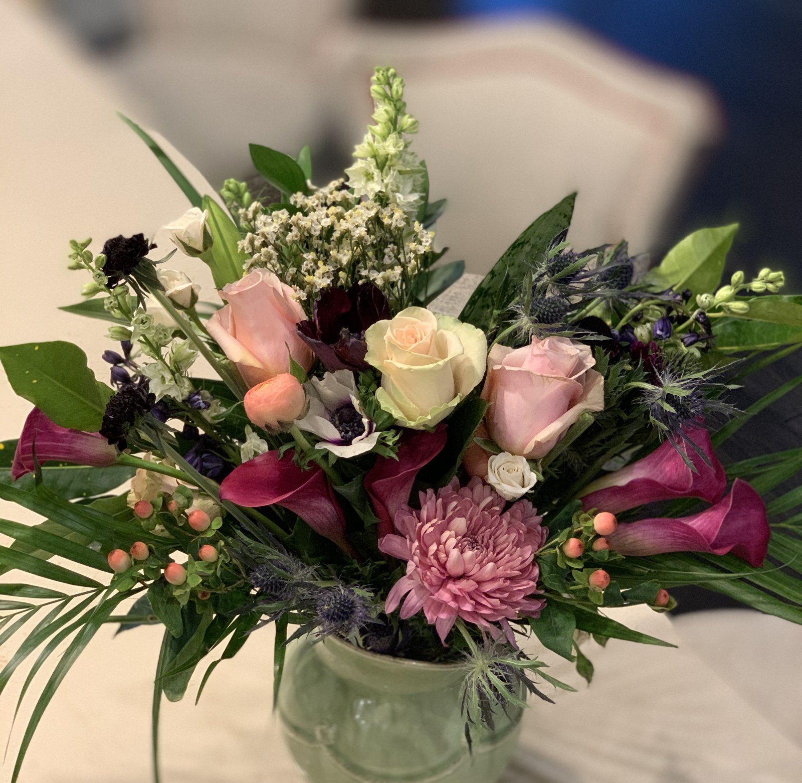 Pink roses, burgundy calla lilies and foliage in a green glass bowl