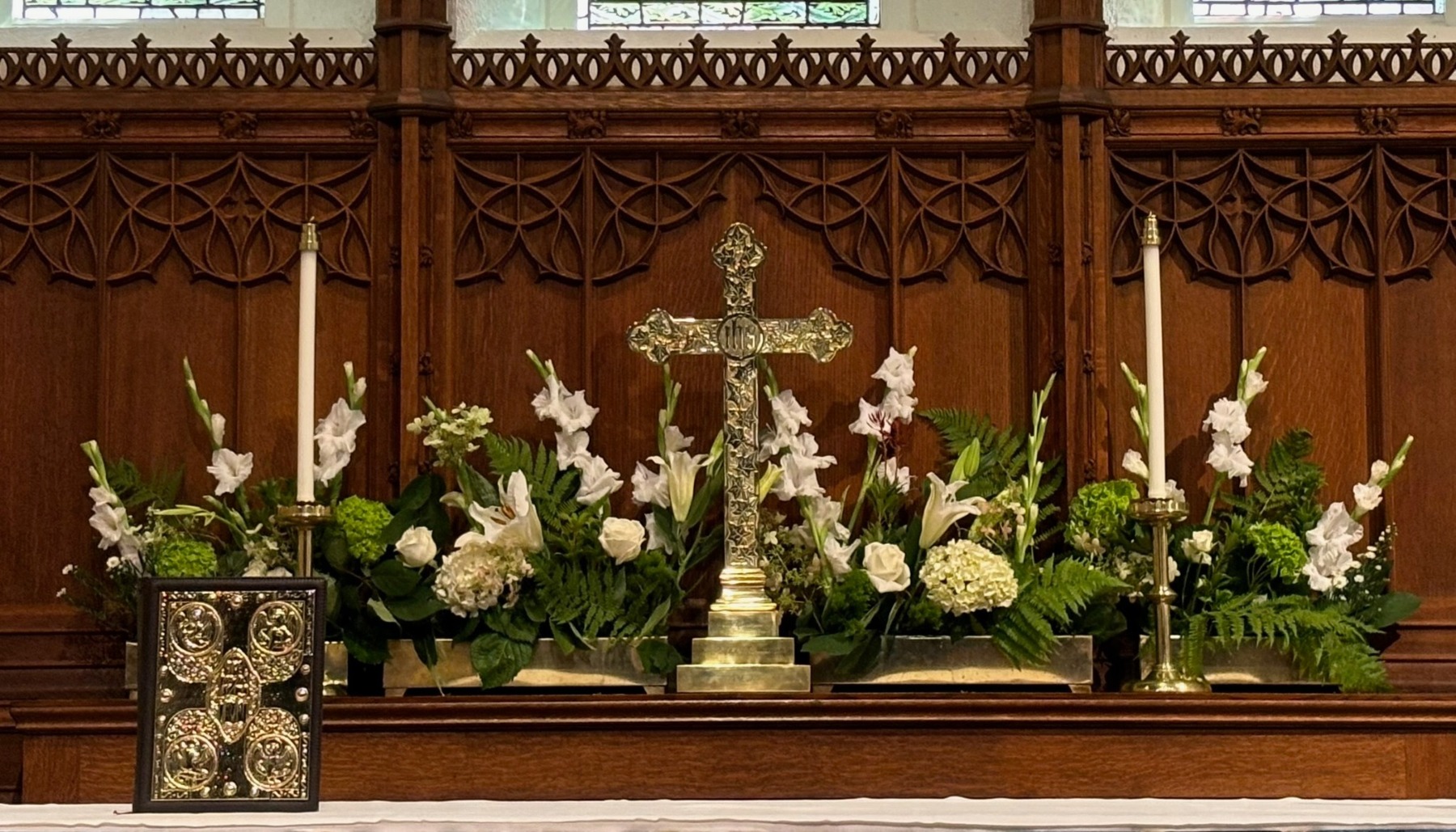 White flowers and green foliage arranged along a carved wooden church altar