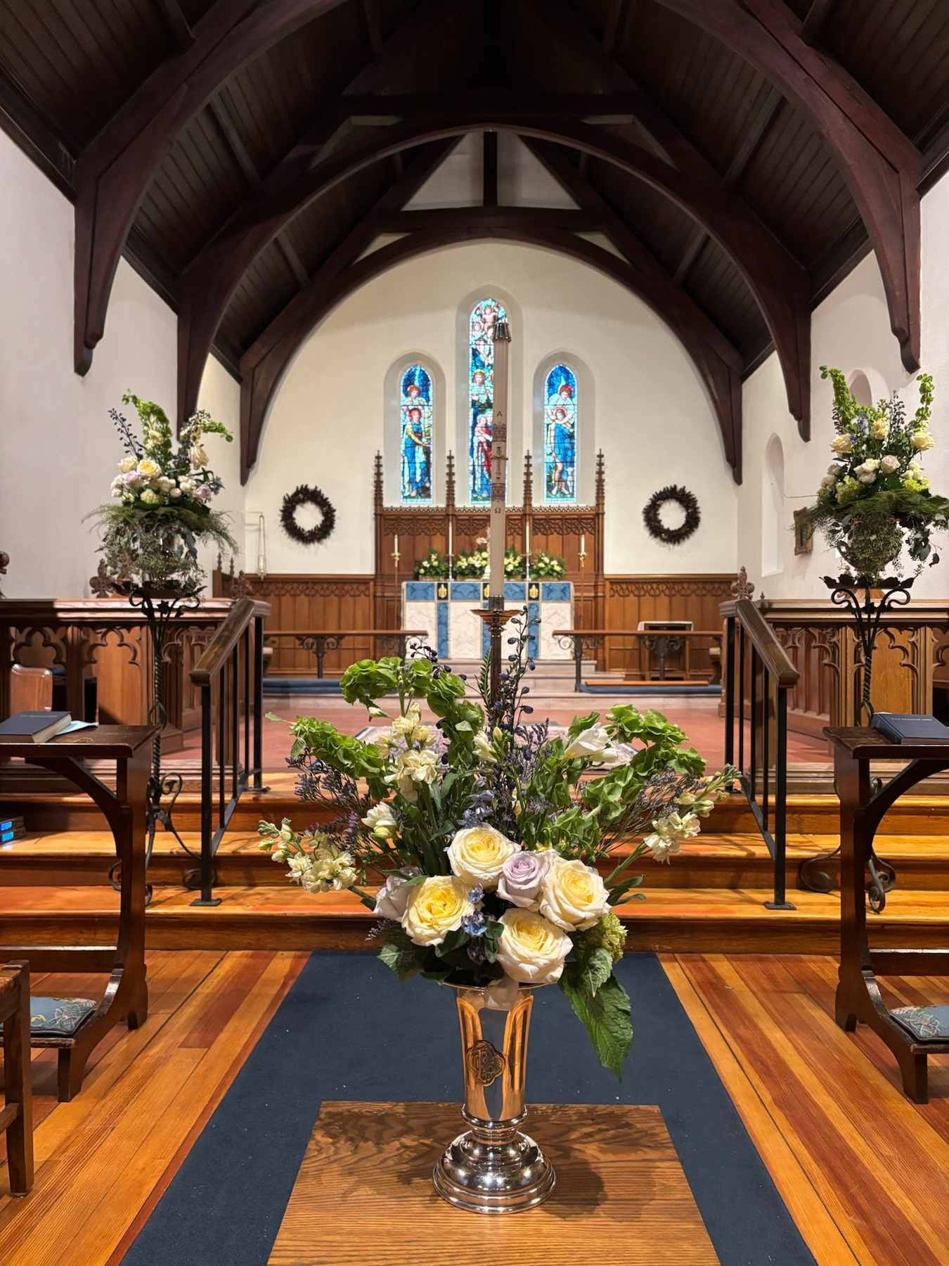 Pale roses and greenery in silver vessels arranged through a church sanctuary
