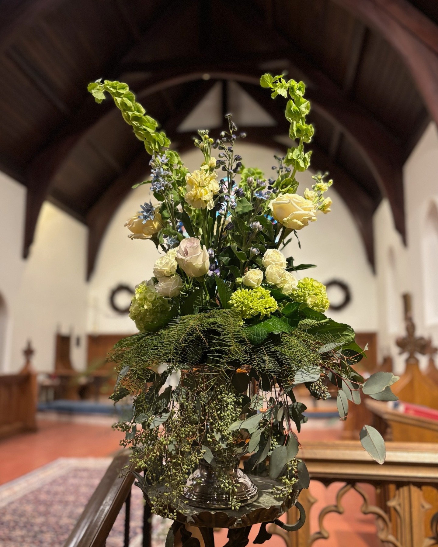Cream and pale pink roses, blue flowers and trailing greenery in a silver vessel