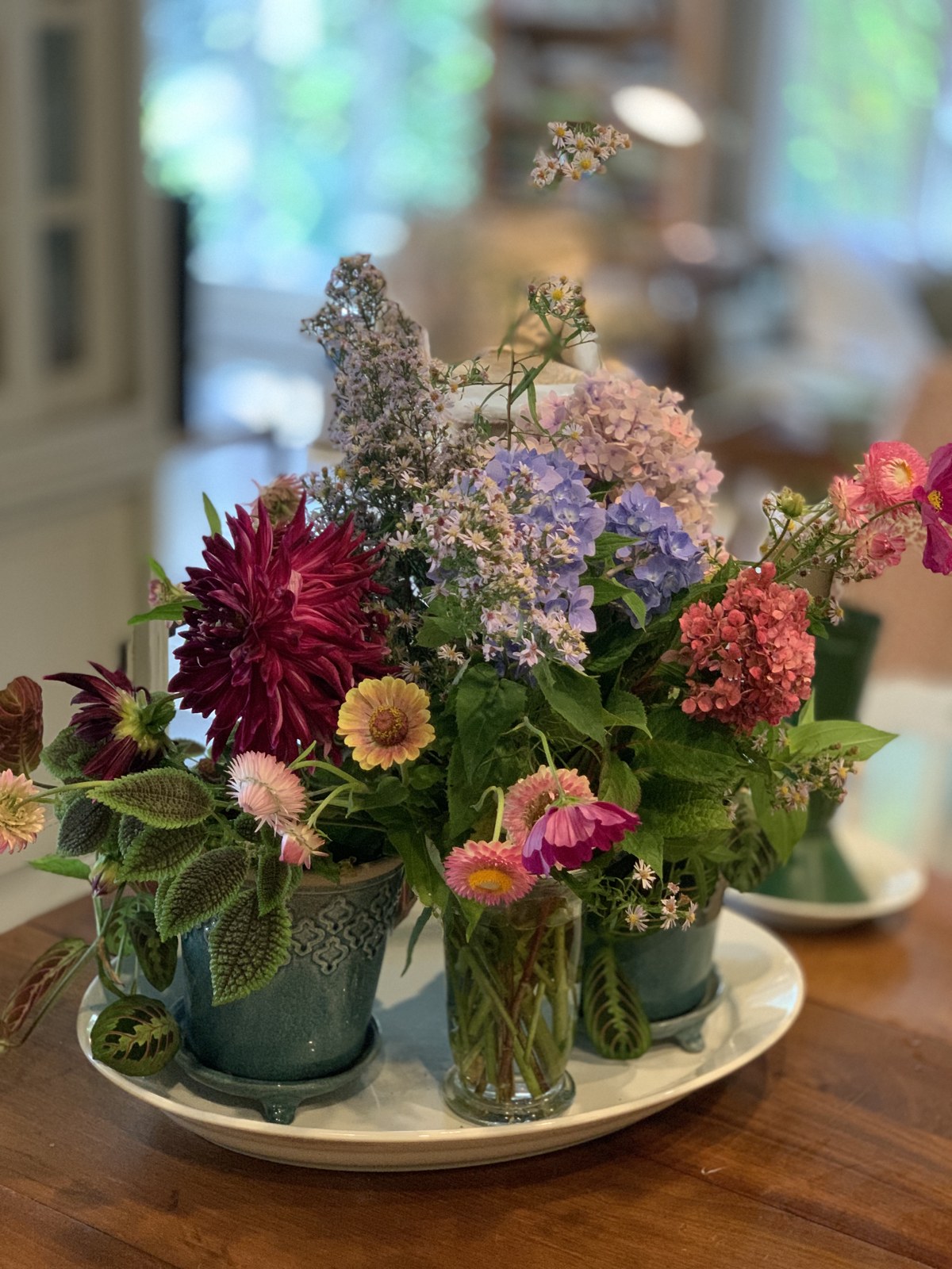 Mixed flowers in three collected green vessels on a tray