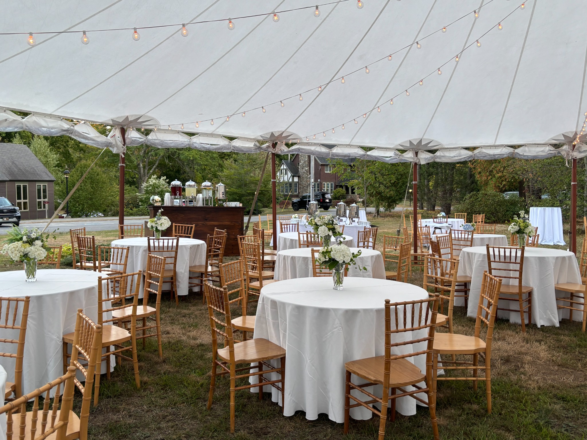 White and blue flowers on reception tables beneath rows of café lights inside the wedding tent
