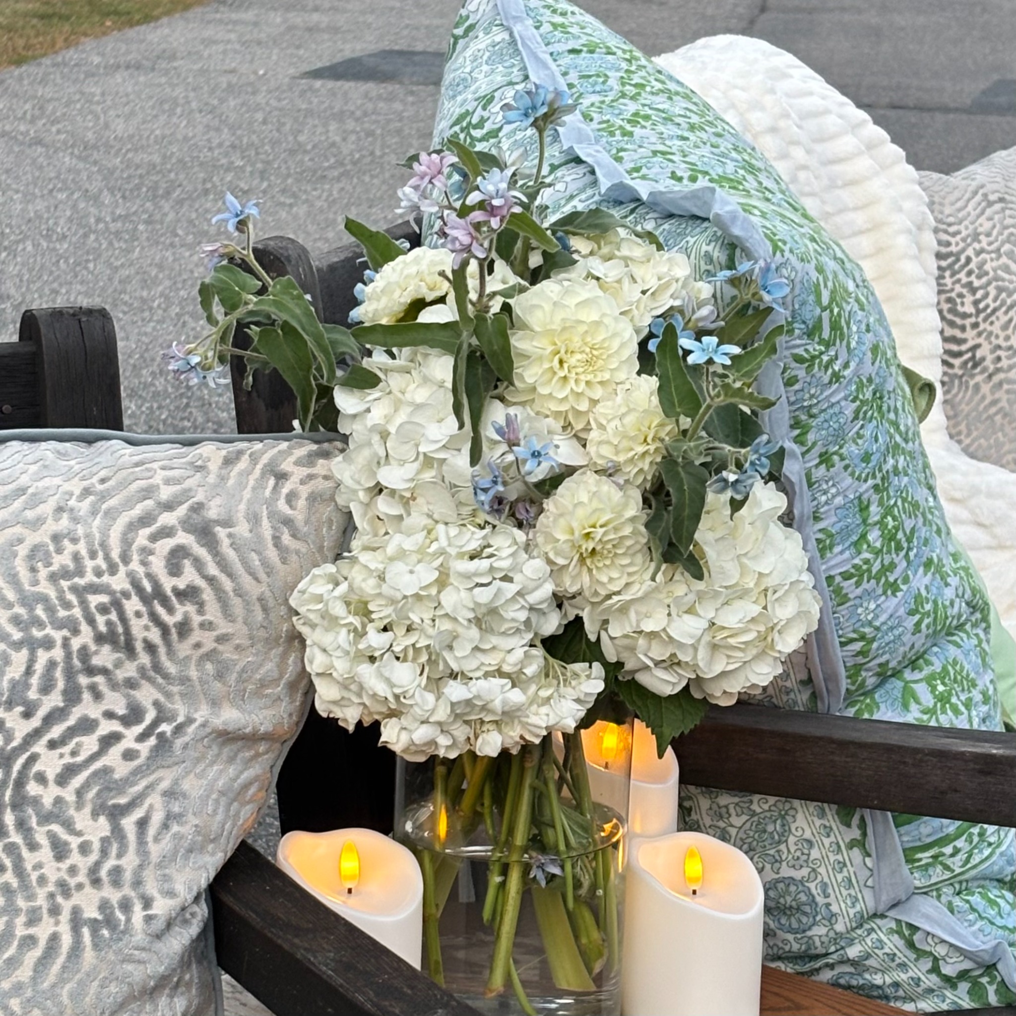 White and blue wedding flowers in a clear vase beside patterned blankets and candles