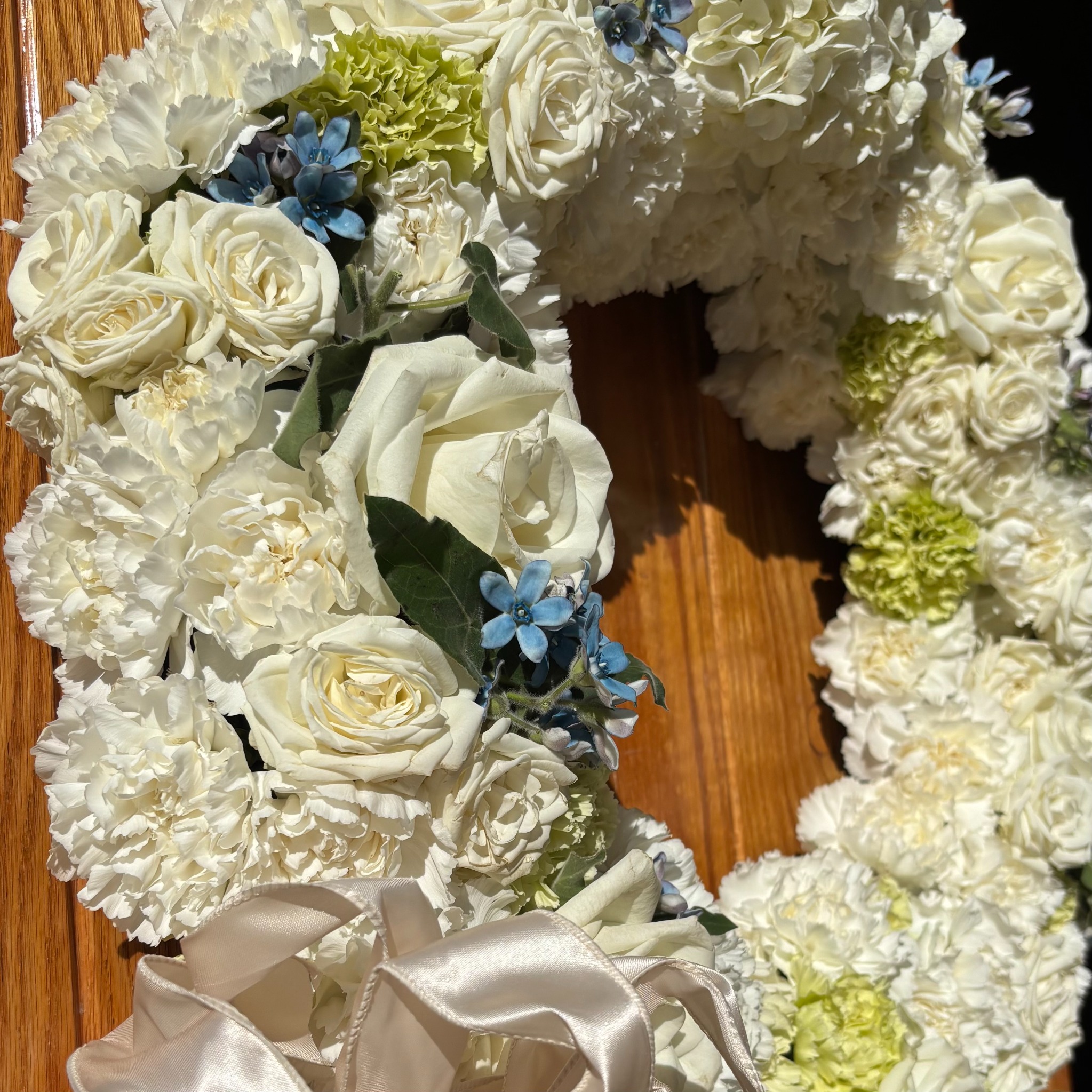 A wedding wreath of white flowers with blue accents and a satin ribbon