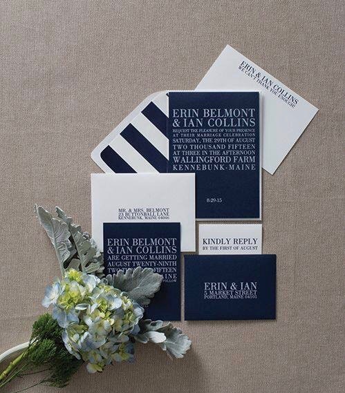 A navy and white wedding invitation suite with striped details beside pale flowers