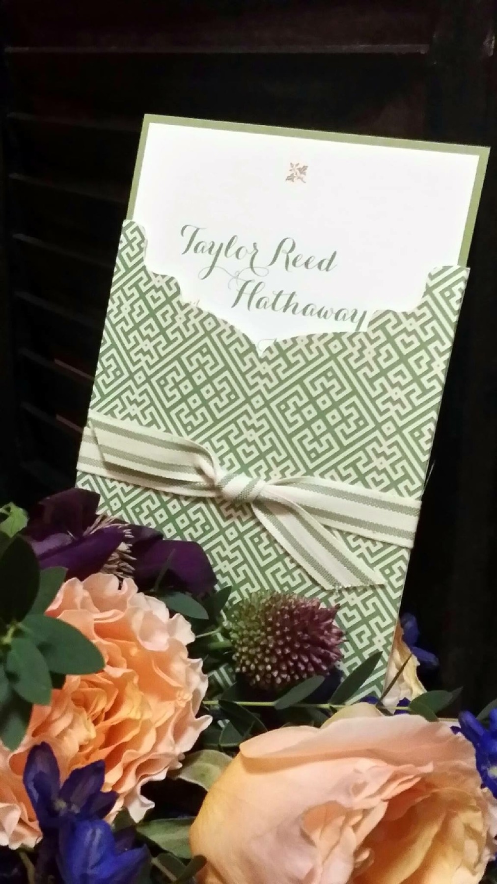 A green patterned wedding program tied with striped ribbon beside flowers