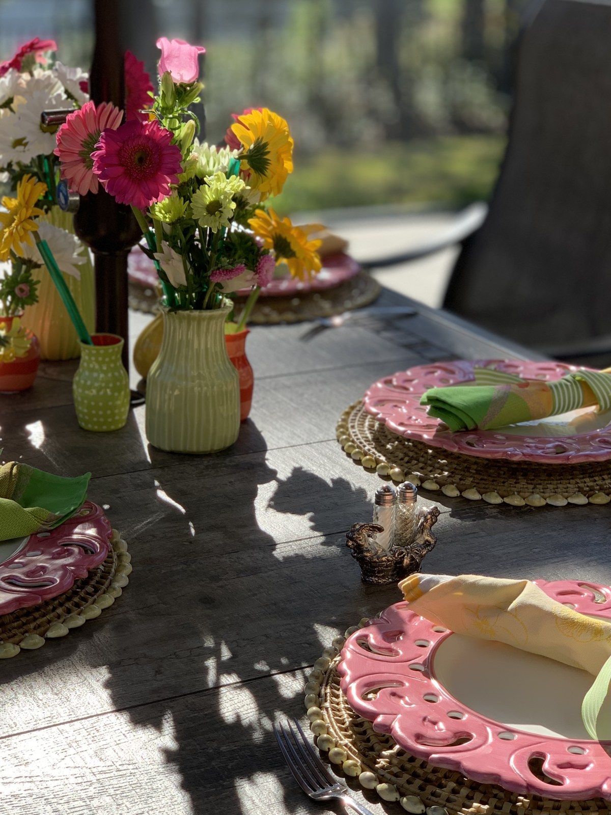 Pink plates, striped napkins and colorful flowers on a sunlit outdoor table
