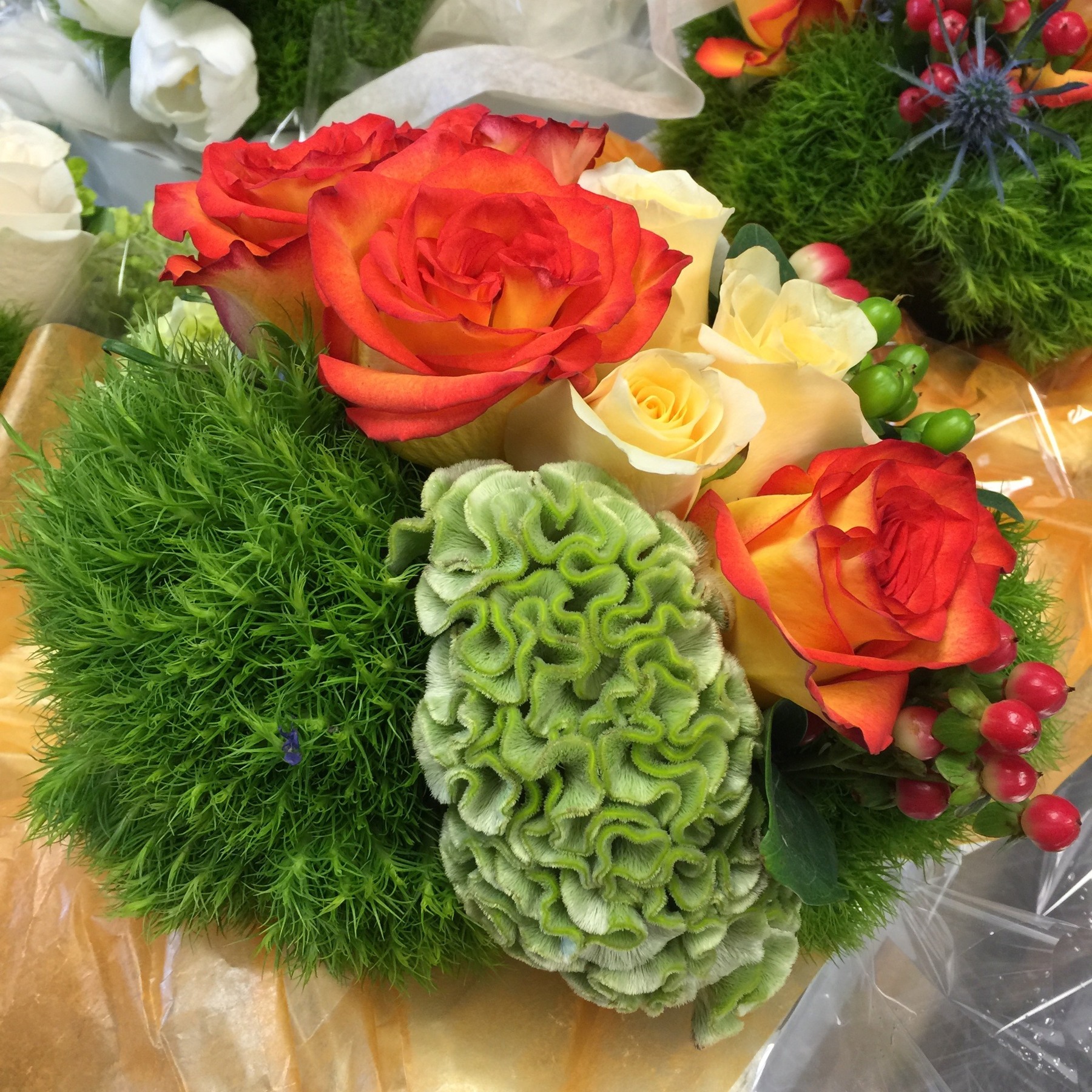 Orange and cream roses with green textured flowers and red berries seen close up