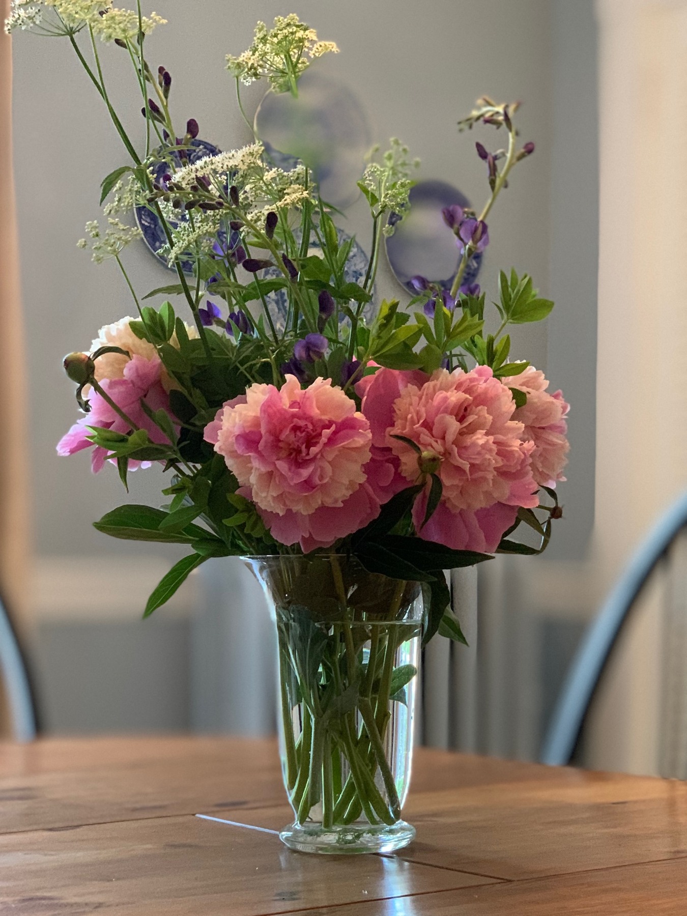 Pink peonies with airy white and purple stems in a glass vase on a wooden table