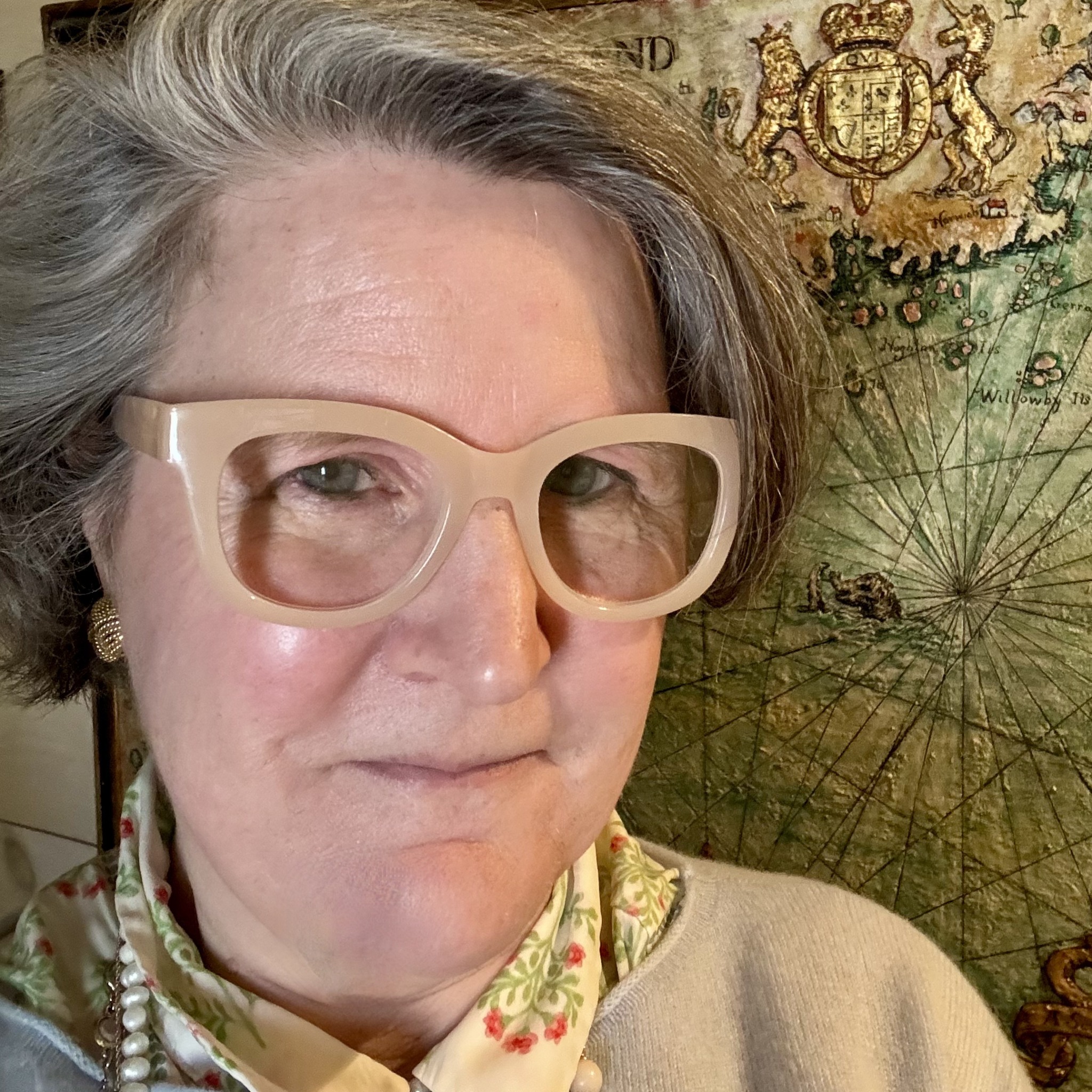 Valerie Kyros wearing cream glasses and a floral scarf beside an antique map