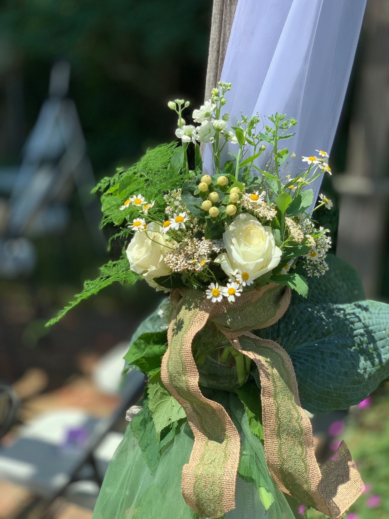 White roses, tiny white flowers and greenery tied to an arbor with trailing fabric