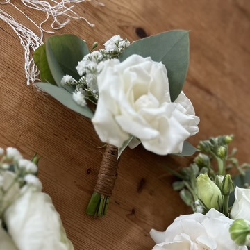 White rose boutonnière with tiny white flowers, green leaves and a wrapped stem