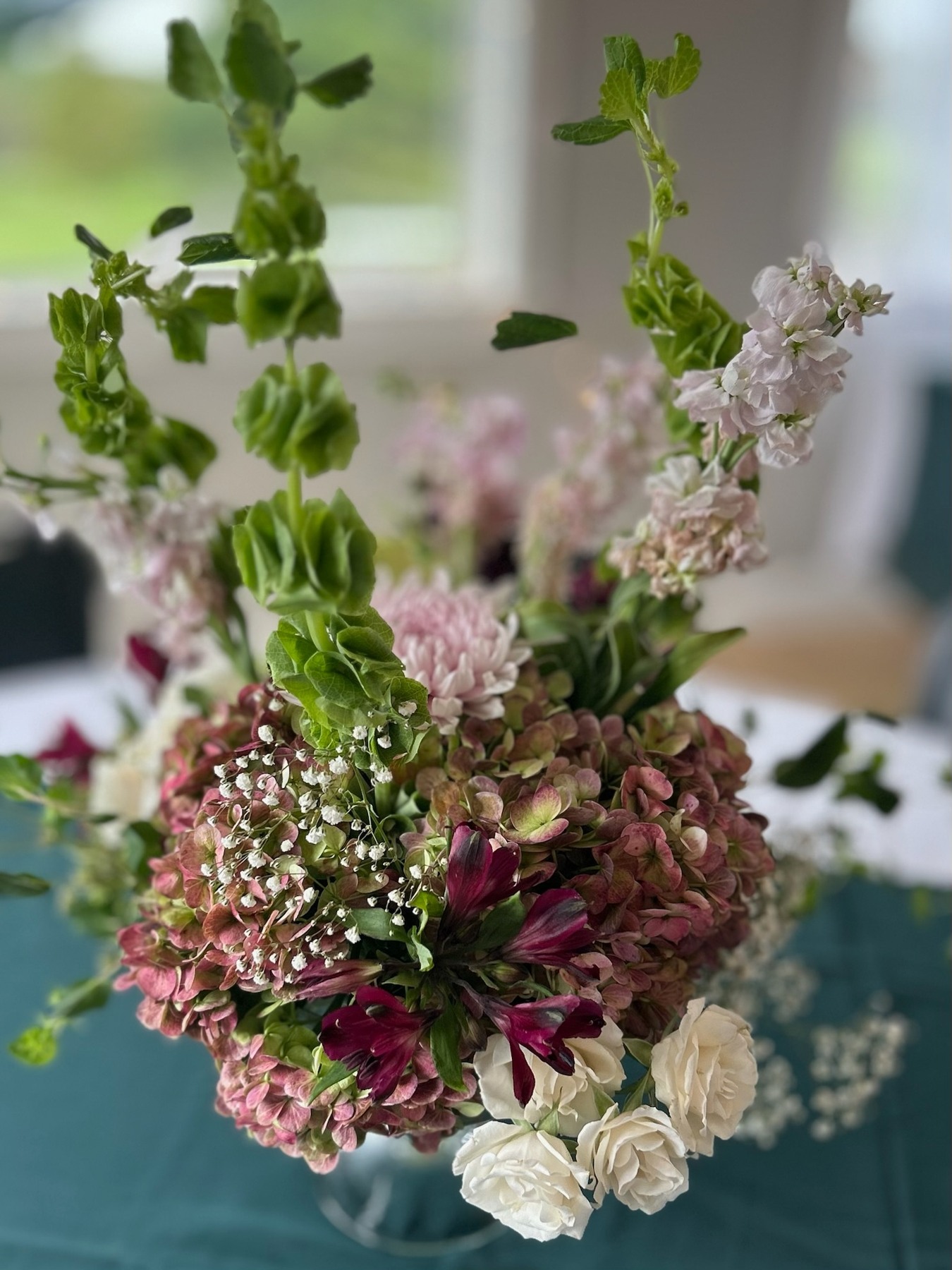 Pink hydrangeas, pale roses and tall green stems in a glass vessel