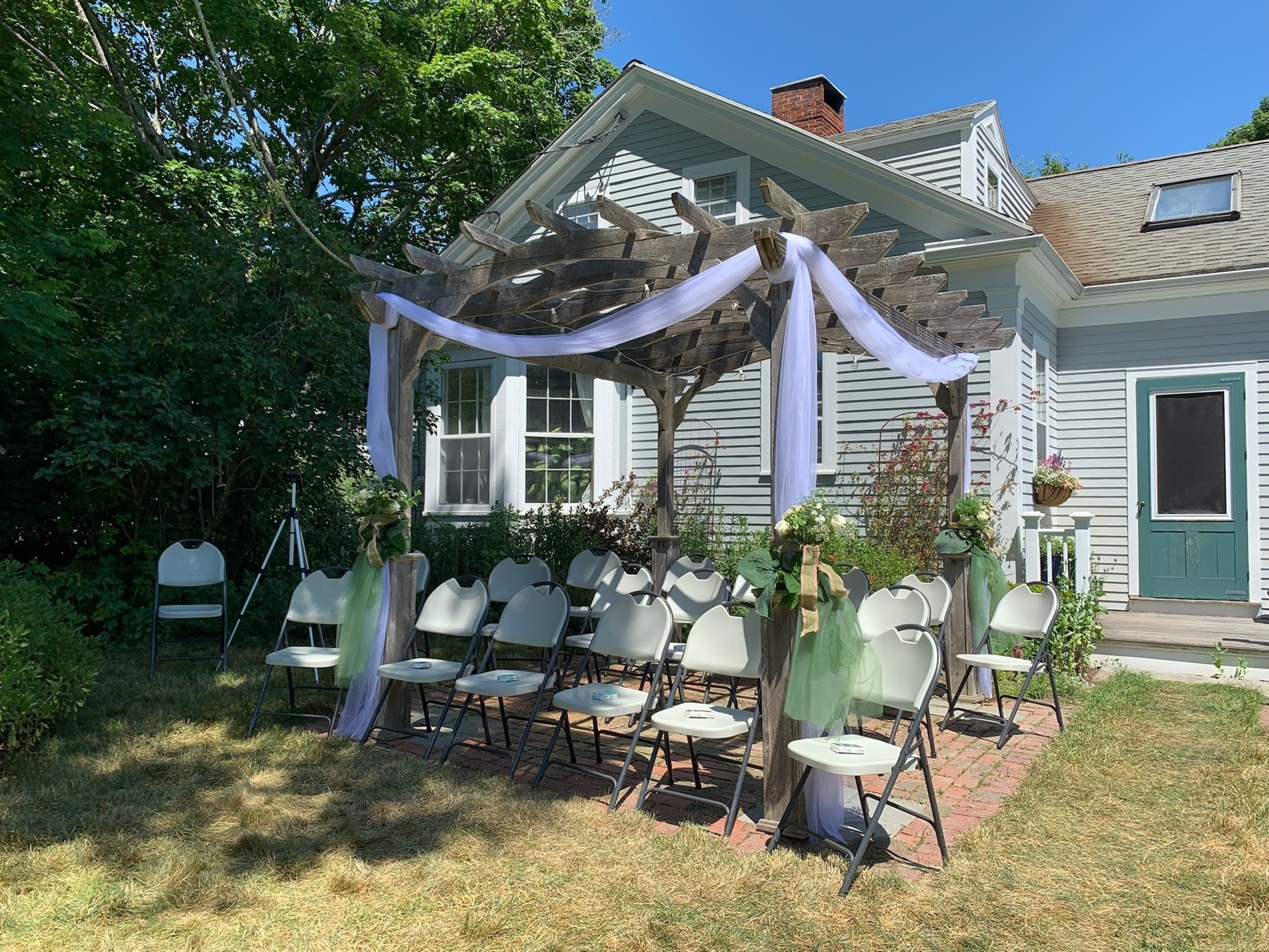 Draped garden arbor and ceremony chairs outside a family home