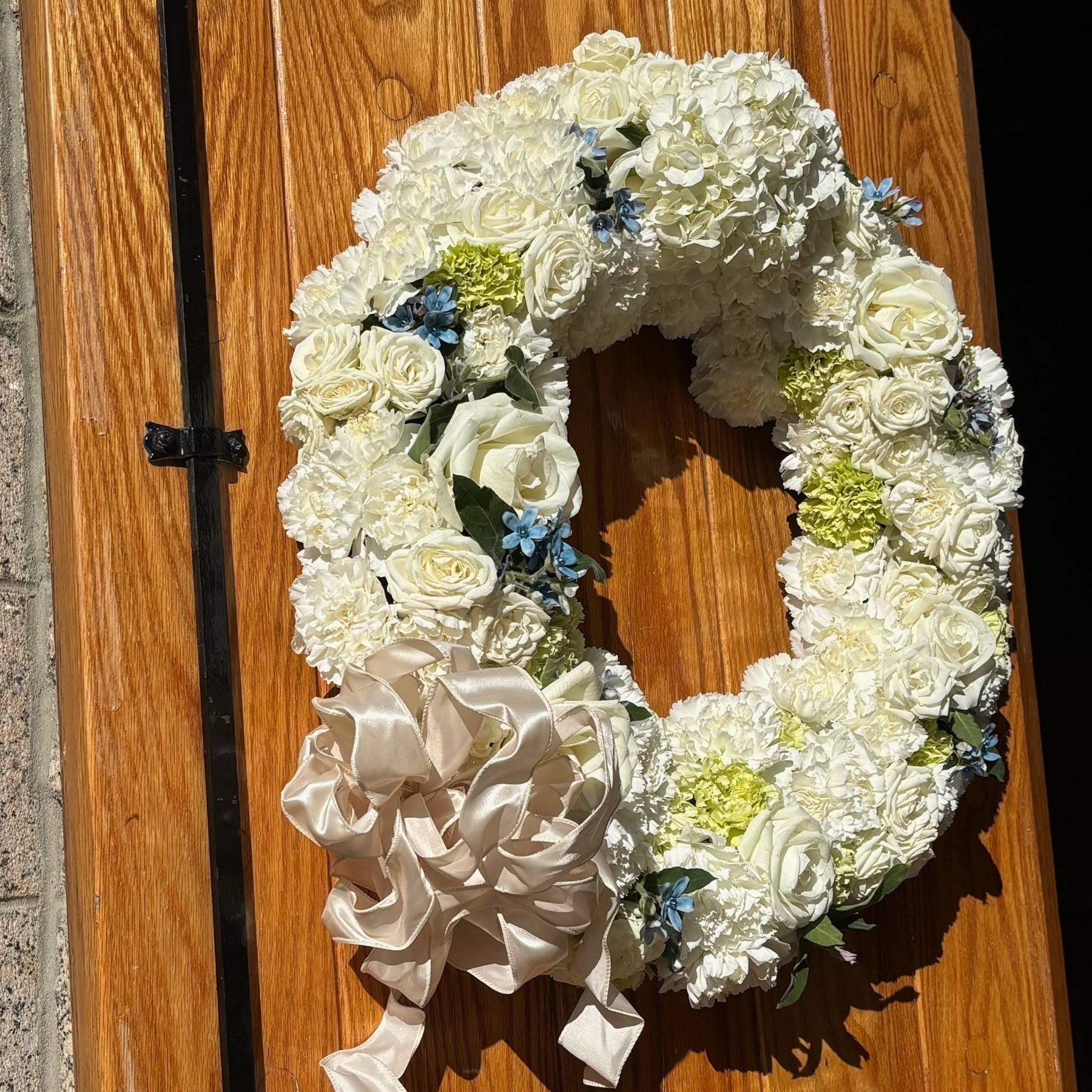 White and pale blue hydrangea wreath with a soft ribbon on a wooden door