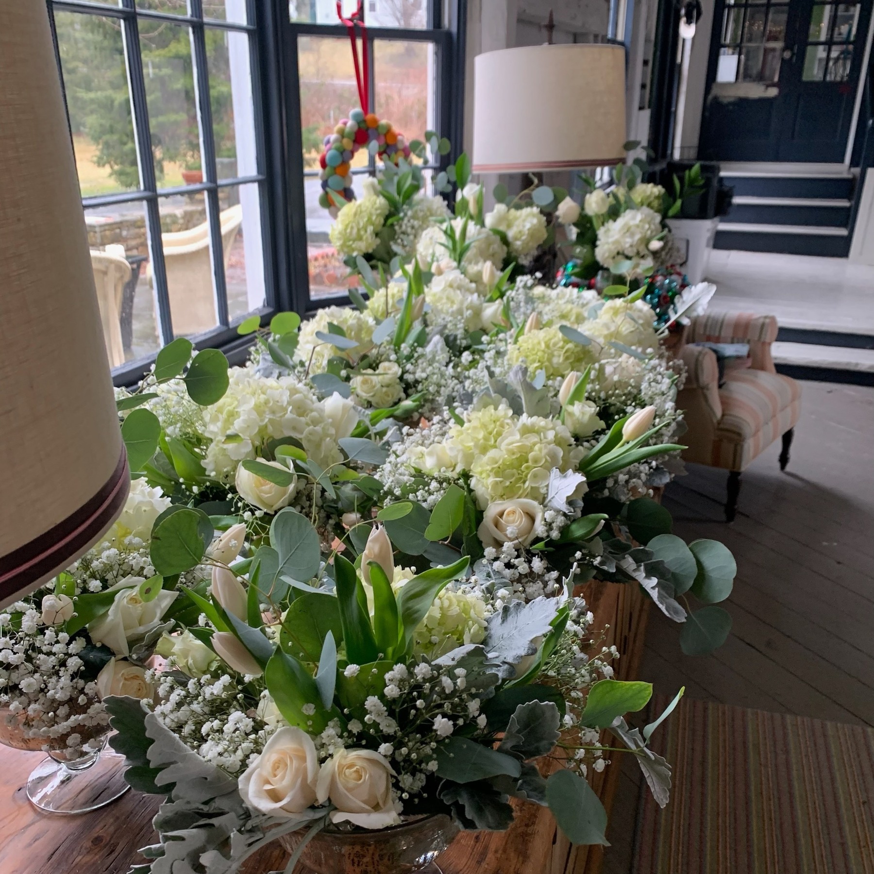 White and green table arrangements grouped beside a window