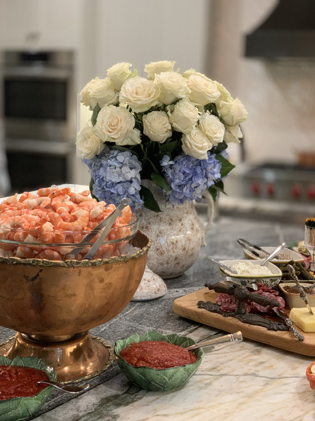 White roses and blue hydrangeas beside food served in copper and collected dishes